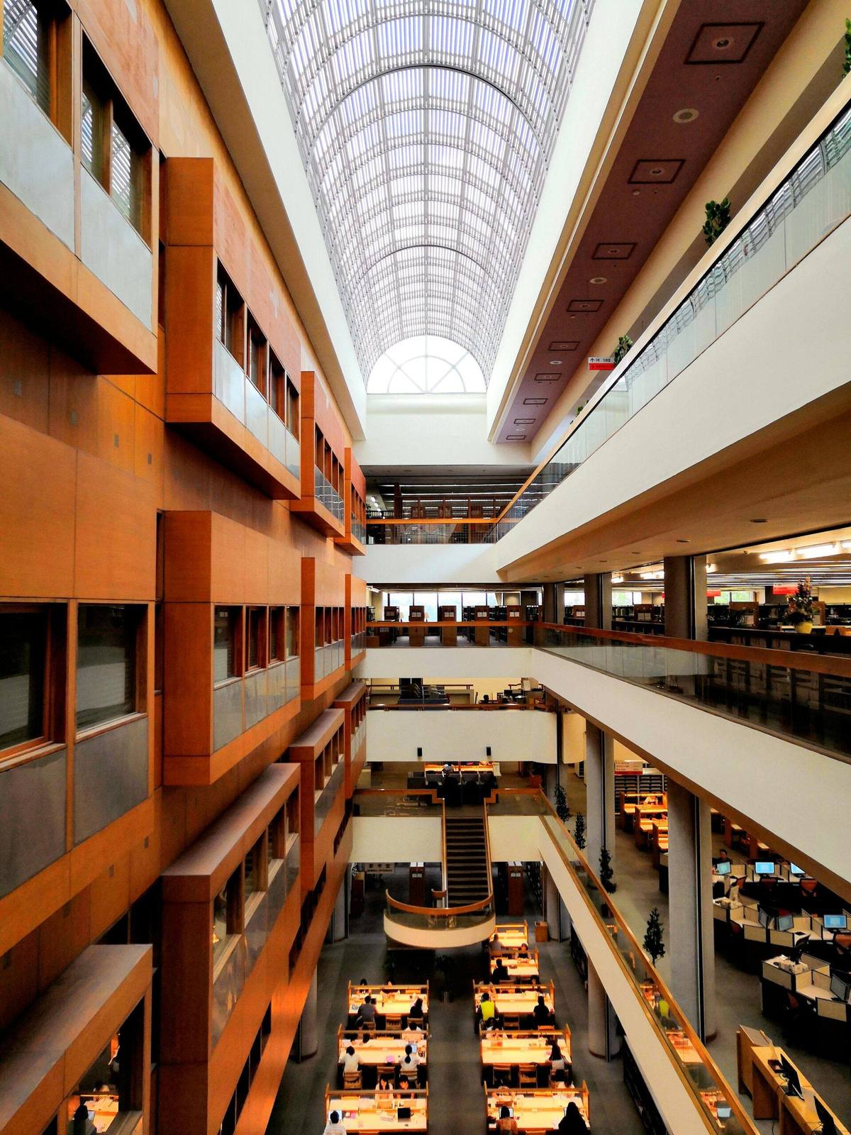 Multi-storey atrium interior with timber-clad walkways under a vaulted glass roof